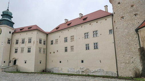 Zdjęcie przedstawia ścianę zamku obok baszty i wieży zegarowej.