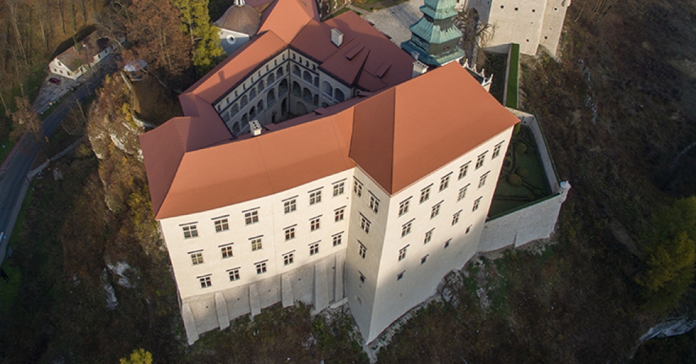 widok z lotu ptaka na mury zamku Pieskowa Skała, jasne tynkowane ściany, czerwony dach, dookoła krajobraz jury krakowskiej