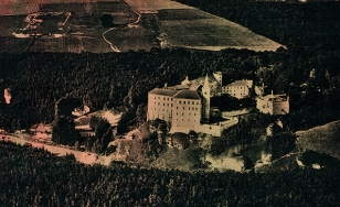 Czarno-biała fotografia przedstawiająca zamek w Pieskowej Skale oraz otaczające go tereny zalesione z lotu ptaka.