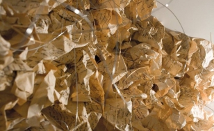 Zbliżenie na fragment instalacji, składający się ze zmiętych, odręcznie zapisanych pożółkłych kartek papieru, połączonych ze sobą i poprzeplatanych cienkim drucikiem. Kształt instalacji przypomina chmurę lub koronę drzewa.