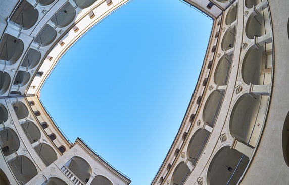 Zdjęcie przedstawia krużganki z perspektywy środka dziedzińca, tworzy wrażenie osaczenia przez budynek.
