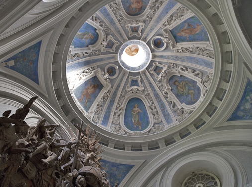Zdjęcie przedstawia wewnętrzną część w kopule kaplicy, zdobiona jest białymi elementami na niebieskim tle, a pośrodku znajduje się otwór wpuszczający promienie słońca, rozświetlające wnętrze.