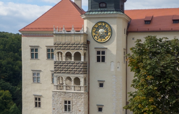 Zdjęcie przedstawia ścianę zamku z wieżą zegarową i zdobioną loggią z arkadami.
