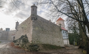 Zdjęcie przedstawia fragment kamiennego muru okalającego zamek. Rogi muru zwieńczone są wieżyczkami.