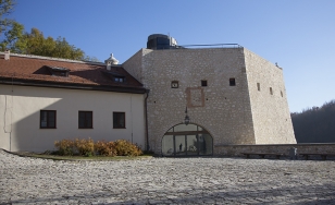 Zdjęcie przedstawia kamienny dziedziniec i 2 budynki - fragmenty zamku.