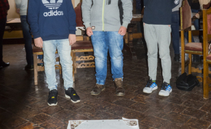 Zdjęcie uczestników wydarzenia z wykonaną przez siebie pracą. Troje chłopców pozuje z projektem plakatu wykonanym techniką kolażu.