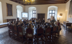Zdjęcie grupowe uczestników wydarzenia, siedzących w kole na ozdobnych krzesłach.