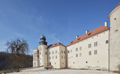 Zdjęcie przedstawia ścianę zamku obok baszty i wieży zegarowej.