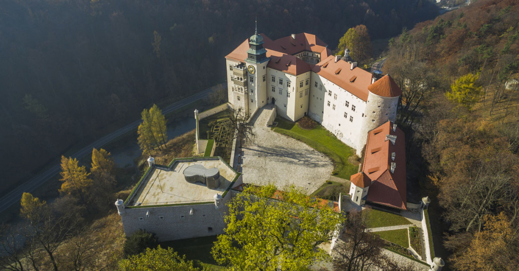 widok z lotu ptaka na zamek, położony malowniczo w dolinie, otoczony lasami